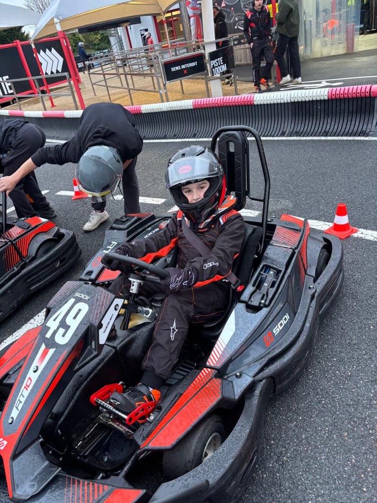 Le jeune pilote casqué au volant d’un kart rouge et noir.
