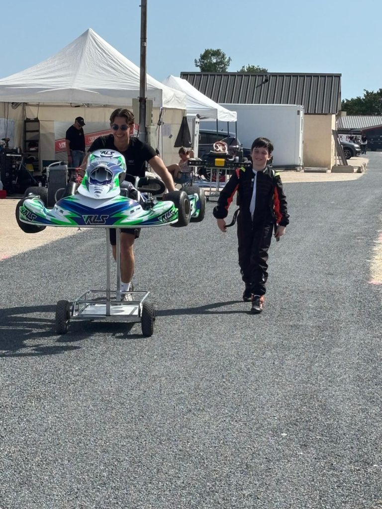 Le jeune pilote marche dans le paddock près d’un kart sur son chariot.