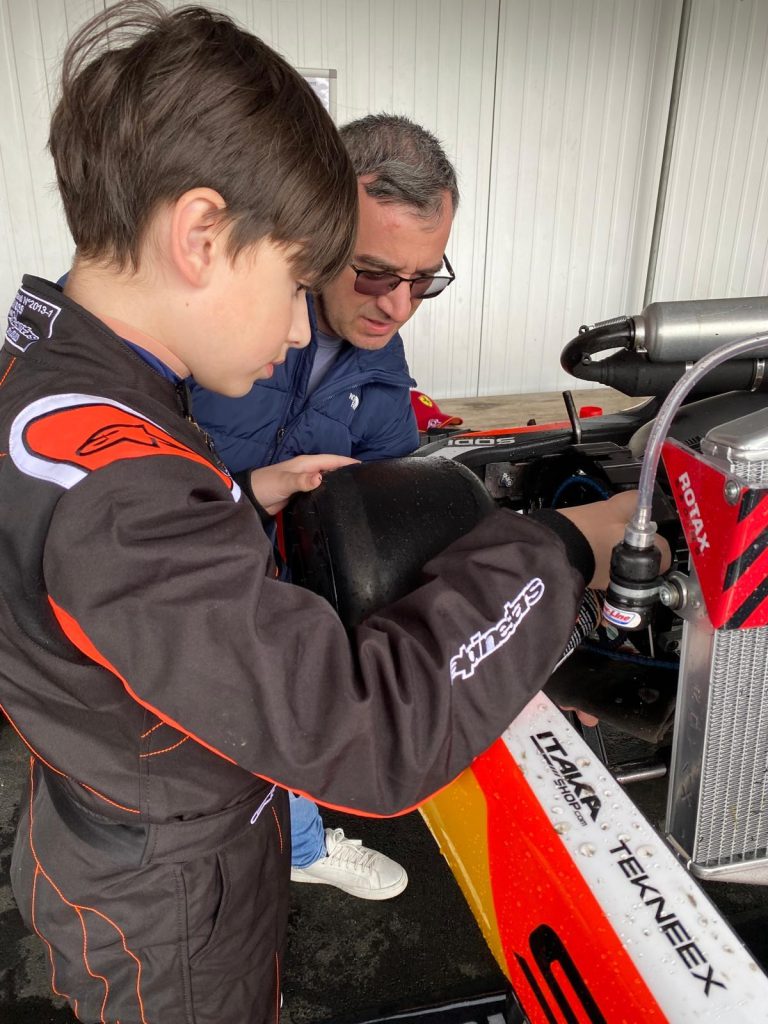 Le jeune pilote observe les éléments mécaniques d’un kart.