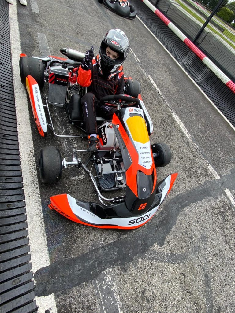 Le jeune pilote casqué salue depuis son kart rouge et noir.