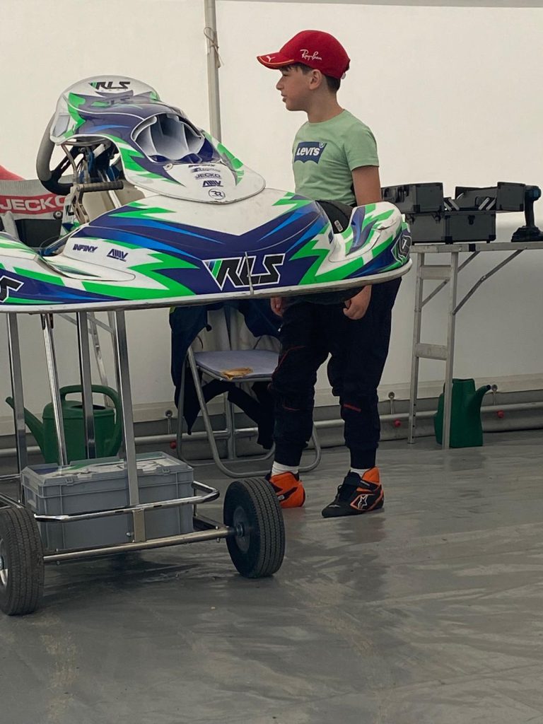 Le jeune pilote près d’un kart et de son casque dans le paddock.