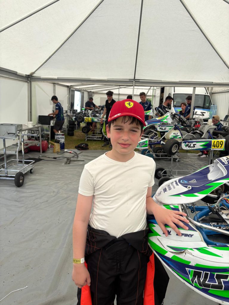 Portrait du jeune pilote près d’un kart bleu, blanc et vert.