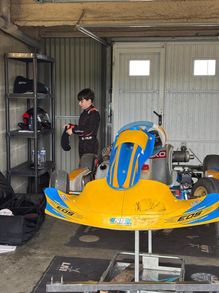 Le jeune pilote en combinaison à côté d’un kart sur son chariot.